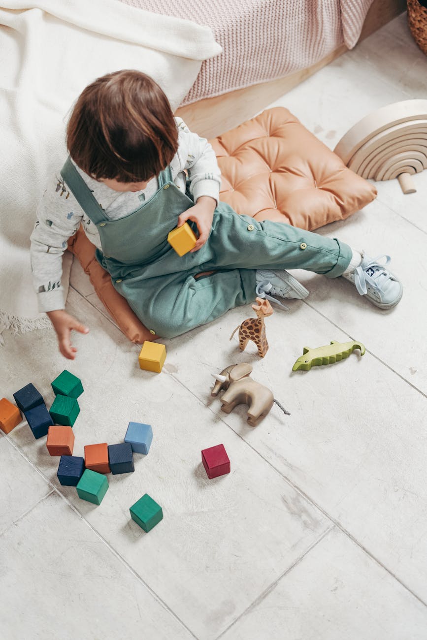 child in white long sleeve top and dungaree trousers playing with lego blocks