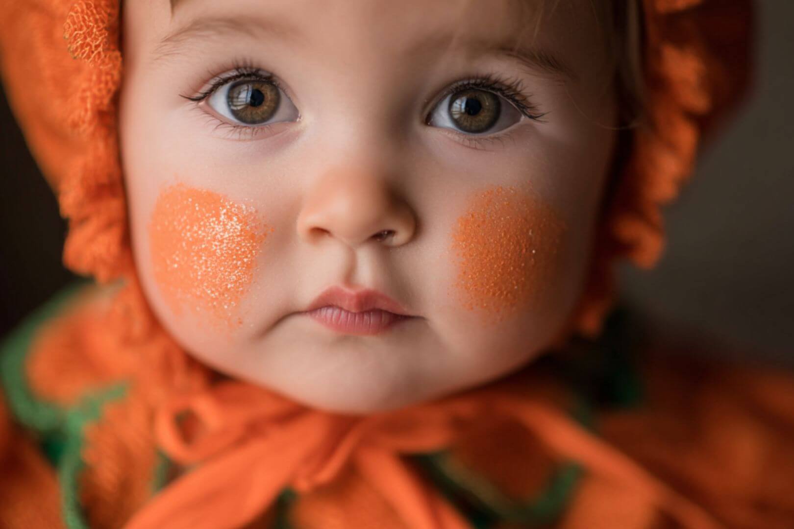 Primer plano de un bebé maquillado y disfrazado de calabaza