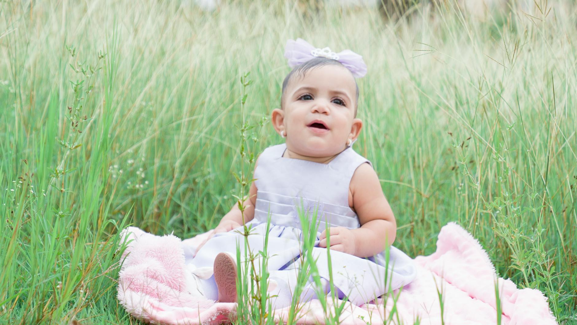 adorable baby girl sitting on blanket in grass field