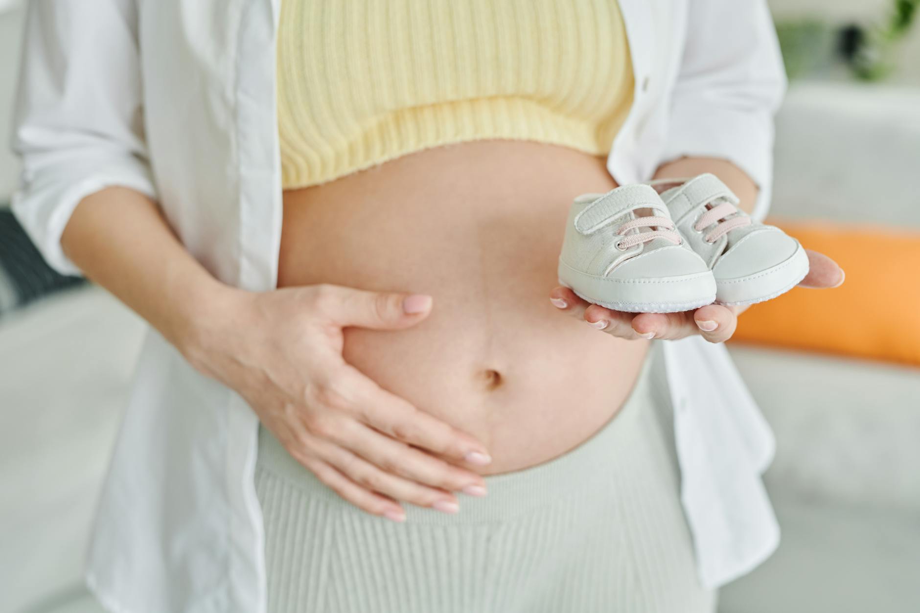 a pregnant woman holding her belly and baby shoes