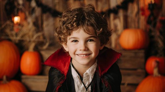 Niño con disfraz casero de vampiro hecho con materiales reciclados y decorado con calabazas de Halloween.