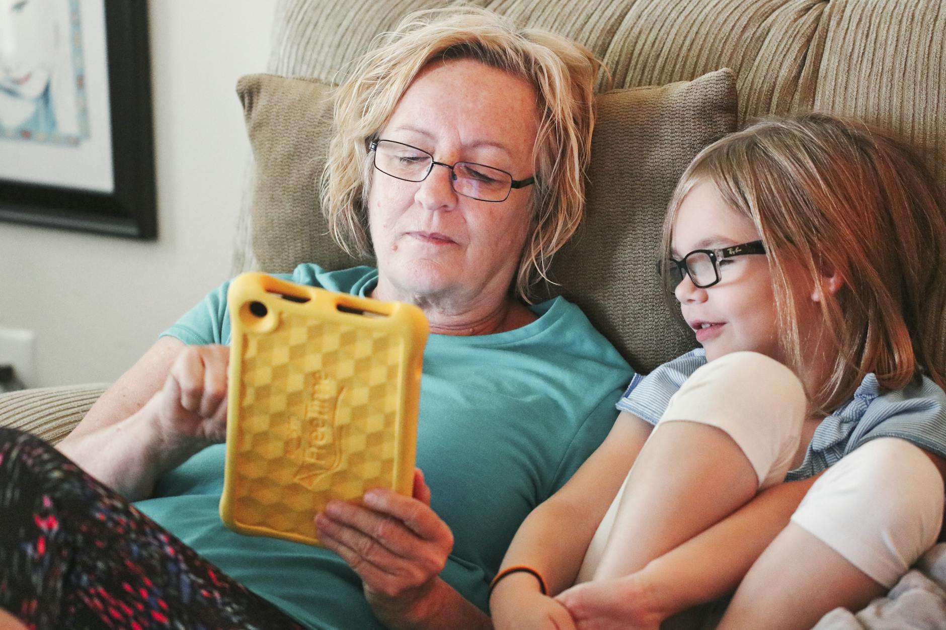 woman holding tablet lying beside girl wear eyeglasses