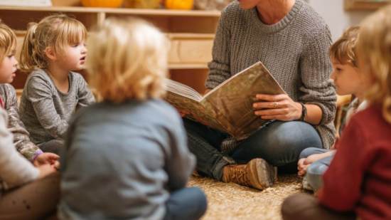 Maestra rodeada de niños en círculo mientras lee un libro en el aula de infantil.