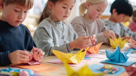 Niños concentrados haciendo figuras de papiroflexia con papeles de colores en clase.
