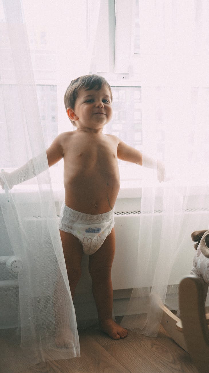 toddler wearing diaper standing near window