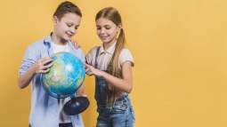 girl-pointing-globe-hold-by-his-friend-against-yellow-background