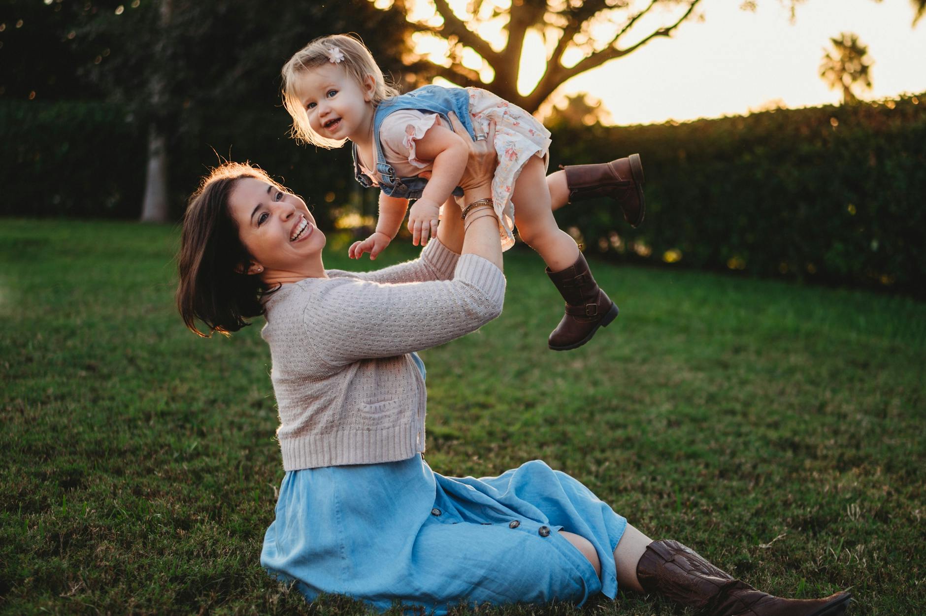 excited woman raising cute daughter on hands in garden
