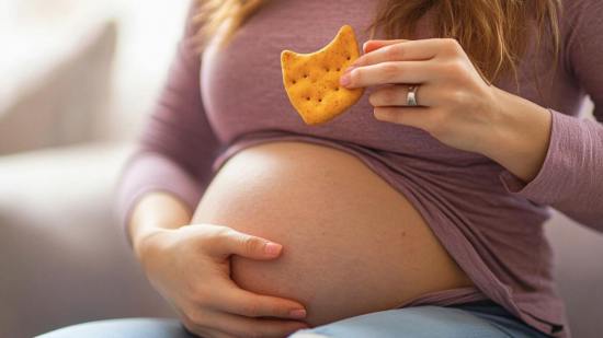 Una mujer embarazada con una galleta en la mano
