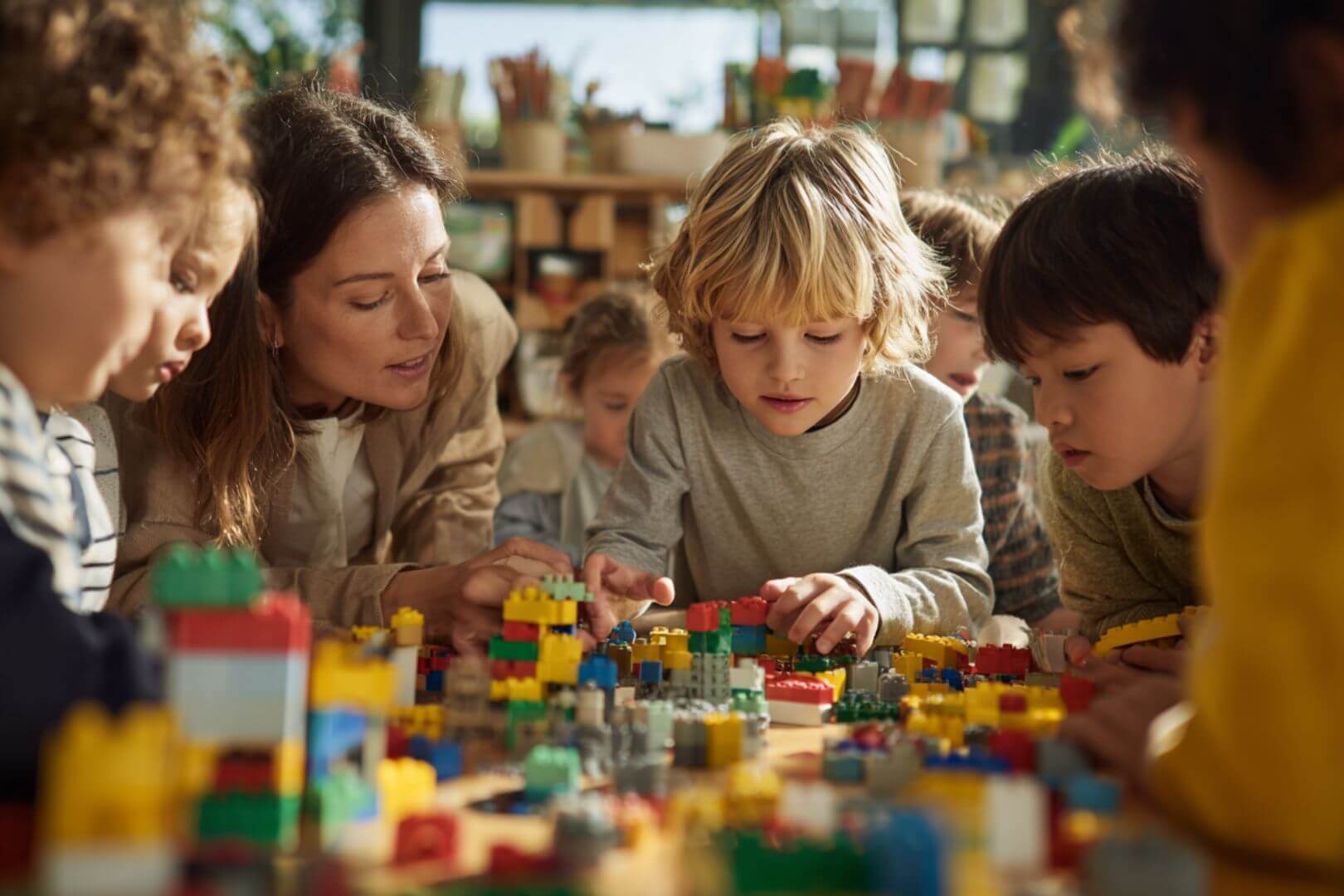 Una docente acompaña el aprendizaje de un grupo de niños mientras construyen con LEGO en el aula.