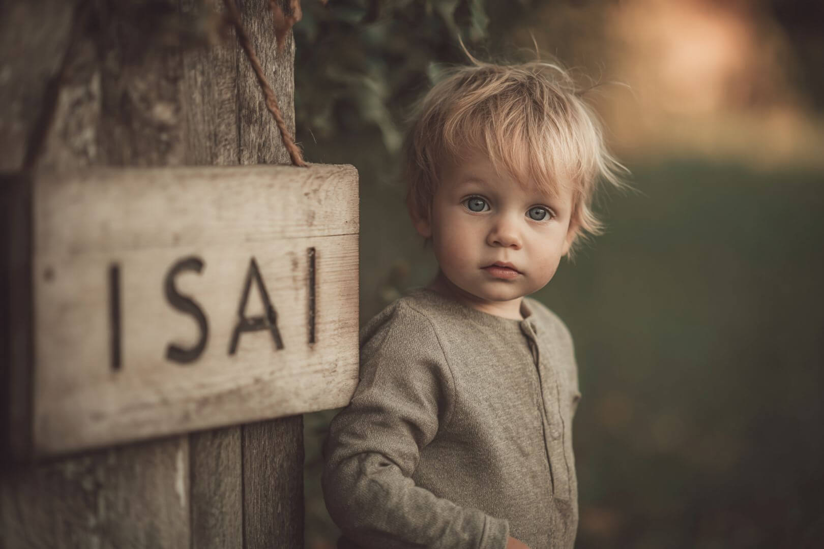 Niño pequeño junto a un cartel de madera con la inscripción ISAI, ambiente cálido y natural