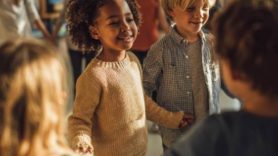 Niños y niñas de infantil cogidos de la mano y sonriendo en clase durante la vuelta al cole.
