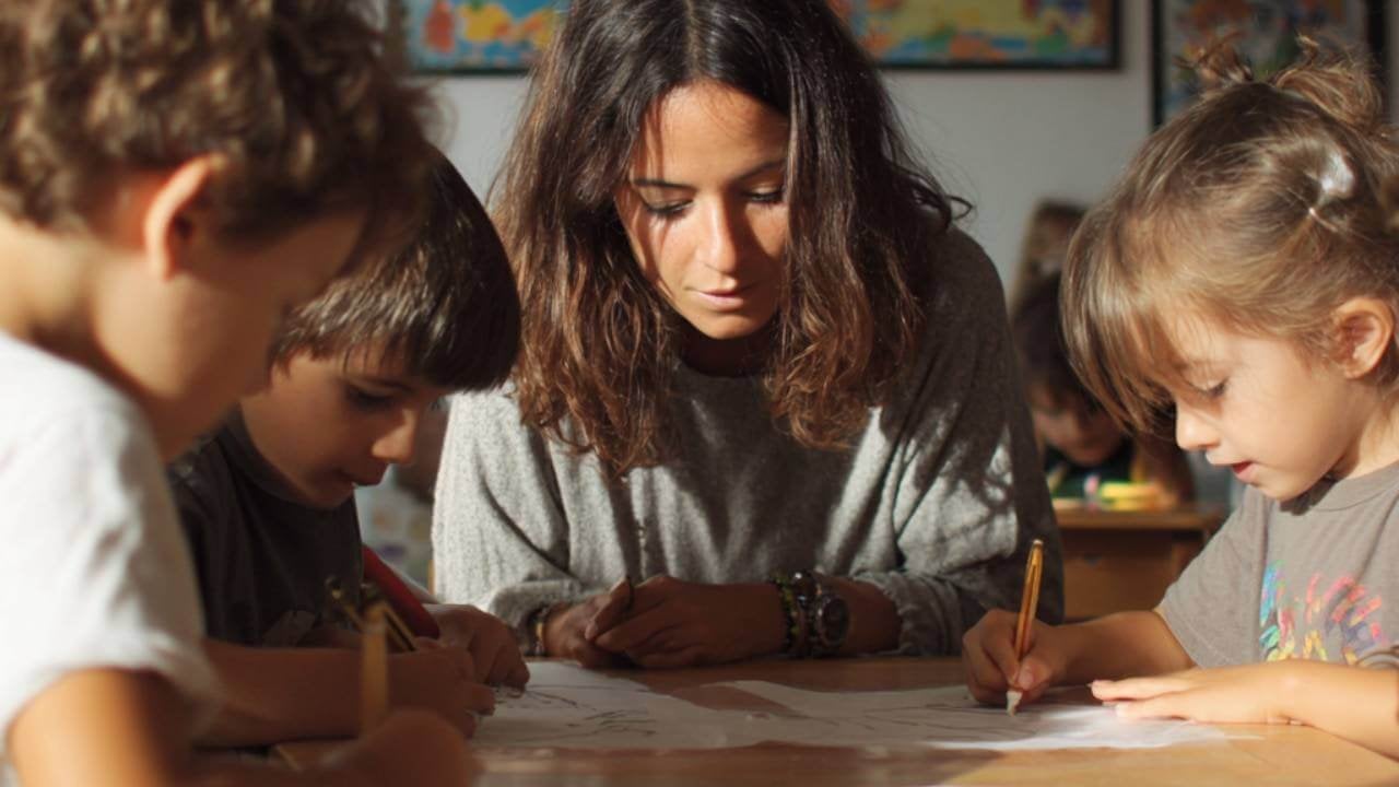 Docente observando a un grupo de niños de primaria mientras trabajan en una actividad creativa en el aula.