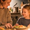 Madre y niño cenando juntos en la cocina, con luz cálida y comida saludable sobre la mesa.