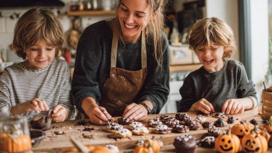 Familia preparando dulces caseros de Halloween con niños, decorando galletas y cupcakes con motivos de calabazas y fantasmas en una cocina otoñal.