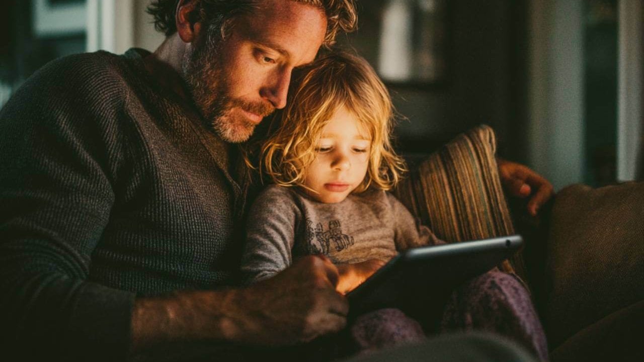 Padre e hijo en casa mientras el adulto ayuda a limitar el uso del móvil con calma y cariño.